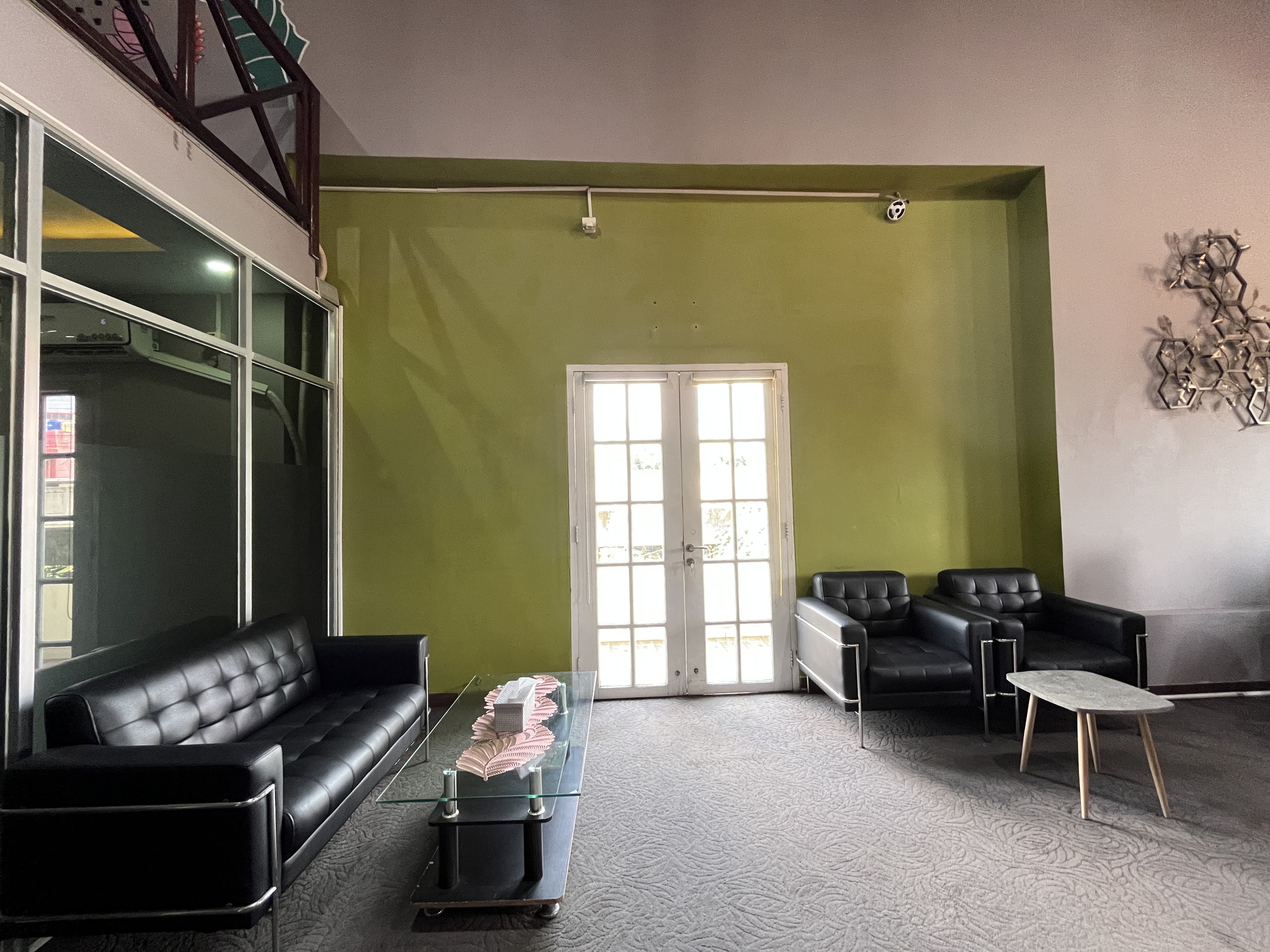 Lounge area with a black leather sofa, two armchairs, a glass coffee table, and a green wall with white glass doors