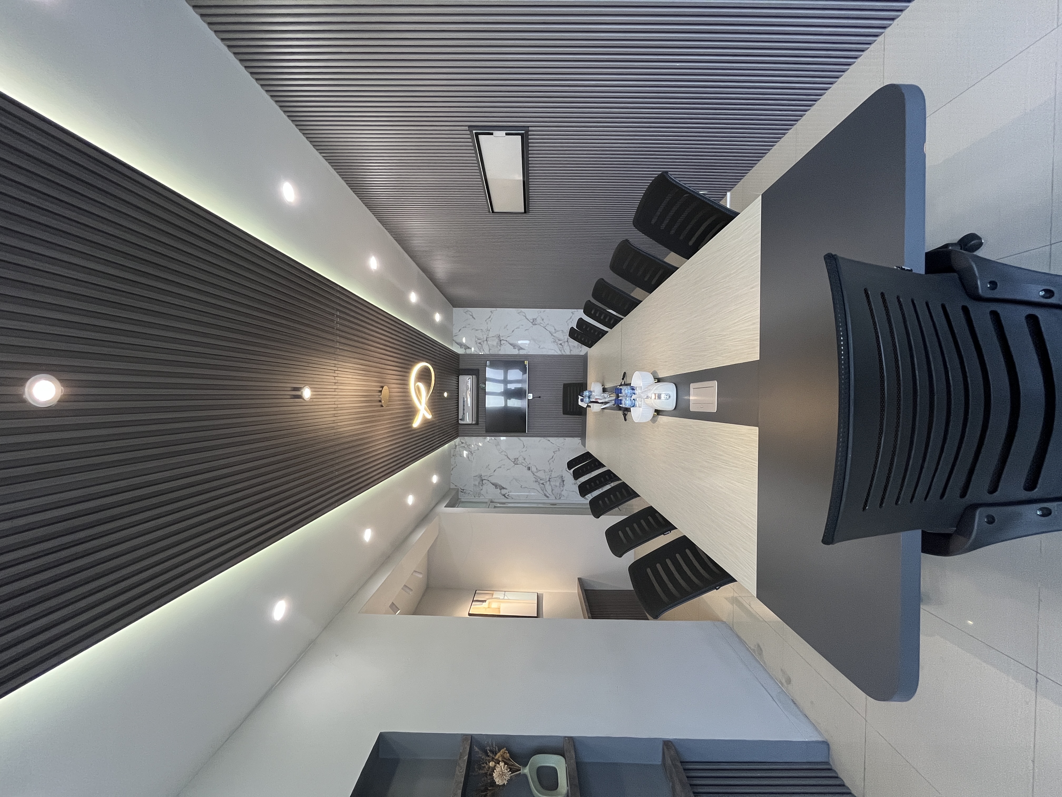 Luxurious meeting room with a long table, rows of black chairs, a slatted wood ceiling with LED lighting, and a wall-mounted TV